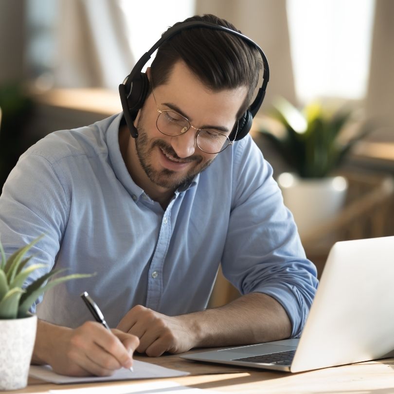 Adult learner smiling and taking notes while attending a virtual meeting